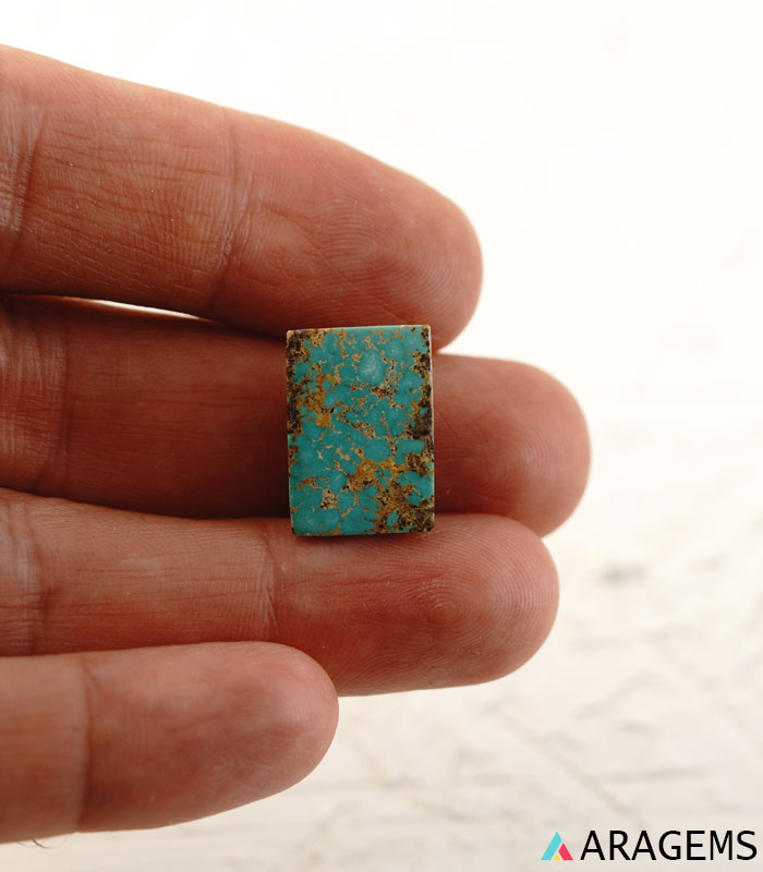 Rectangular Iranian turquoise cabochon shown on hand to display real-life size.