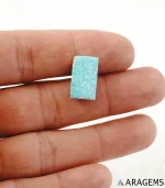 Hand holding natural Kerman turquoise rectangular cabochon showing its 10 x 17 mm size - T43