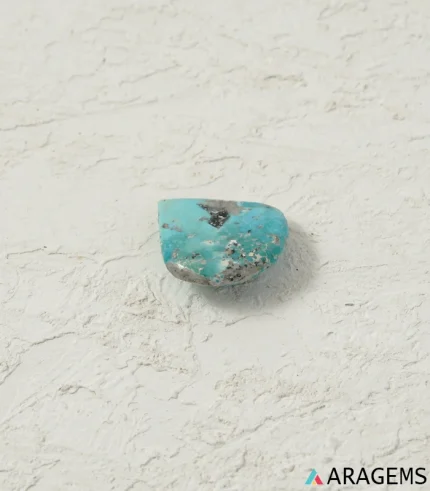 Natural blue Kerman turquoise teardrop cabochon on a textured white surface, close angle - T51