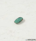 Natural green Kerman turquoise oval cabochon on a textured white surface, angled view - T49