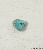 Natural Kerman turquoise teardrop cabochon on a textured white surface, side angle - T51