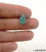 Natural Kerman turquoise oval cabochon on a textured white surface, side angle - T49