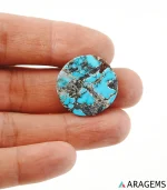 Hand holding natural Neyshabur turquoise round cabochon showing its 23 mm size - T42