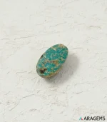 Natural green Neyshabur turquoise oval cabochon on a textured white surface, angled view - T44