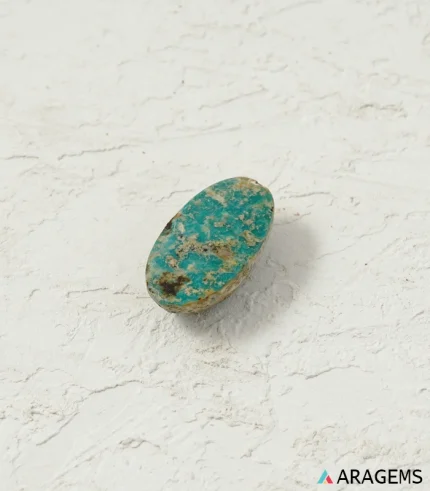 Natural green Neyshabur turquoise oval cabochon on a textured white surface, angled view - T44
