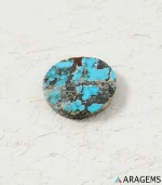 Natural Neyshabur turquoise round cabochon on a textured white surface, angled view - T42