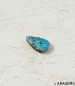 Natural blue Neyshabur turquoise teardrop cabochon on a textured white surface, angled view - T47