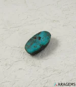 Natural Neyshabur turquoise elongated oval cabochon on a textured white surface, angled view - T50