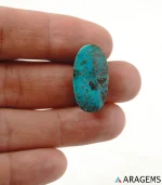 Natural teal-blue Neyshabur turquoise oval cabochon on a textured white surface, side angle - T50