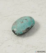 Natural Kerman Persian turquoise oval cabochon on a textured white surface, side angle - T55