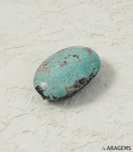 Natural Kerman Persian turquoise oval cabochon on a textured white surface, side angle - T55