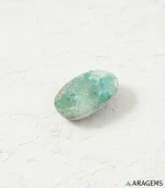 Natural Kerman Persian turquoise oval cabochon on a textured white surface, angled view - T57