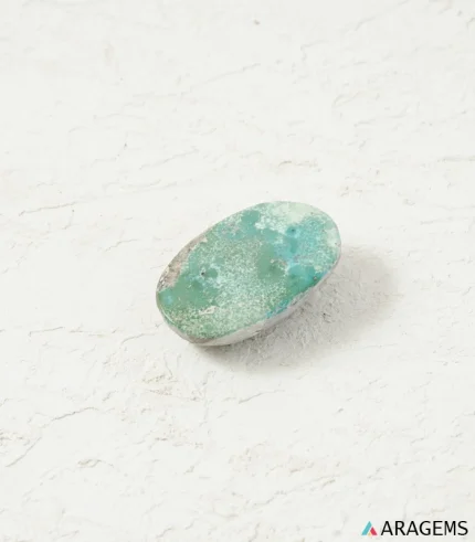Natural Kerman Persian turquoise oval cabochon on a textured white surface, angled view - T57