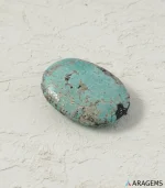 Natural green Kerman Persian turquoise oval cabochon on a textured white surface, close angle - T55