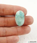 Hand holding natural green Kerman Persian turquoise oval cabochon showing its 16 x 26 mm size - T57
