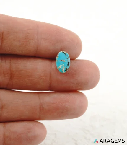 Hand holding natural blue Neyshabur turquoise oval cabochon showing its 7 x 11 mm size - T46