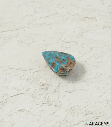Natural Neyshabur turquoise teardrop cabochon on a textured white surface, side angle - T54