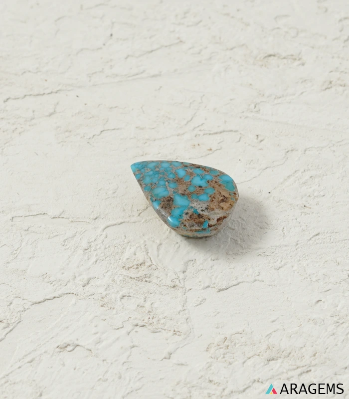 Natural Neyshabur turquoise teardrop cabochon on a textured white surface, side angle - T54