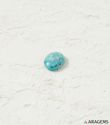 Natural Neyshabur Persian turquoise oval cabochon on a textured white surface, top view - T56