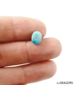 Hand holding natural blue Neyshabur Persian turquoise oval cabochon showing its 8 x 10 mm size - T56