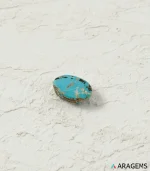 Natural Persian turquoise oval cabochon from Neyshabur on a textured white surface, side angle - T46