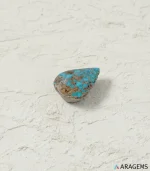 Natural blue Neyshabur turquoise teardrop cabochon on a textured white surface, profile view - T54