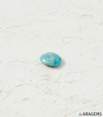 Natural blue Neyshabur Persian turquoise oval cabochon on a textured white surface, angled view - T56